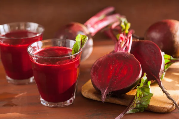 Foto mostra beterrabas cortas e dois copos de suco com beterraba