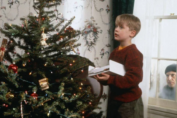 FOTO COLORIDA DE MENINO LOIRO MEXENDO EM ARVORE DE NATAL ENQUANTO É OBSERVADO POR HOMEM NA JANELA - METRÓPOLES