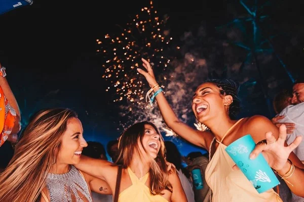 Três jovens mulheres em noite se divertindo com fogos de artifício ao fundo