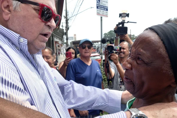 Homem grisalho, com óculos vermelho, em frente à mulher negra - Metrópoles