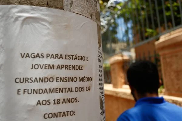Fotografia colorida de um cartaz colado em poste e pessoa de costas ao lado