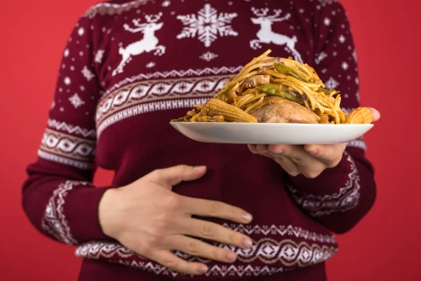 Foto colorida com fundo vermelho e uma mulher segurando um prato enorme de comida - Metrópoles.