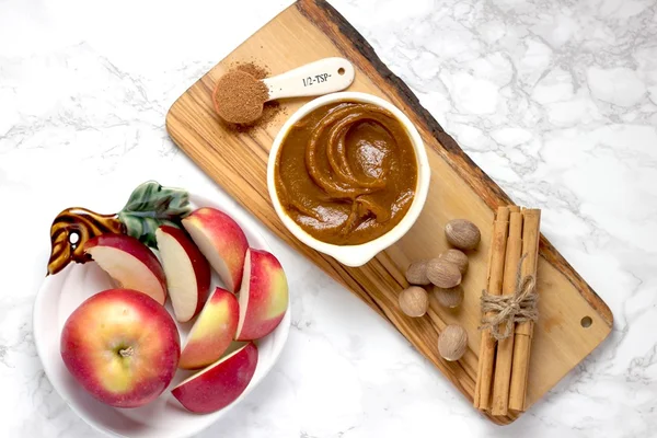 Foto colorida de uma vasilha com frutas e uma tábua de madeira com manteiga de amendoim