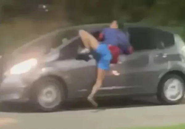 Imagem colorida de homem pendurado e arrastado em carro em movimento - Metrópoles