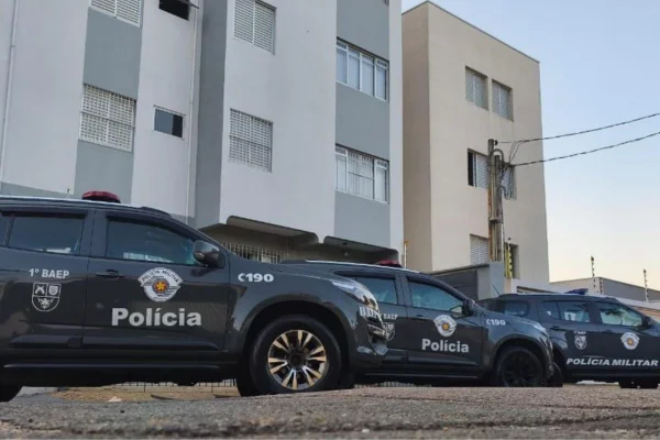 Foto colorida de viaturas da Polícia Militar em frente à imóvel ligado a investigados.