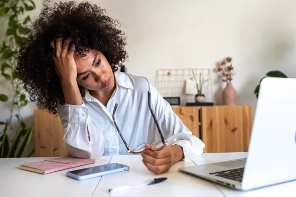 Jovem afro-americana sentindo-se exausta e deprimida sentada em frente ao laptop. Síndrome de burnout no trabalho. Conceito de saúde mental. Metrópoles