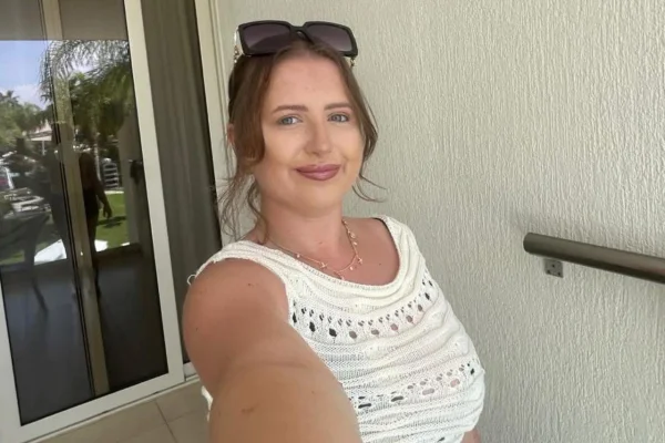 Foto colorida de mulher jovem vestida com blusa branca e óculos de sol na cabeça. - Metrópoles.
