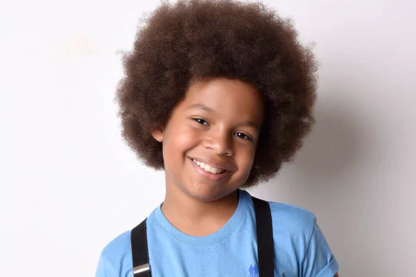 Foto colorida do ator mirim Levi Asaf. Criança negra de cabelo black power, veste uma blusa azul - Metrópoles