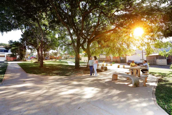 Fotografia mostrando pessoas caminhando e conversando em uma mesa de uma praça-Metrópoles