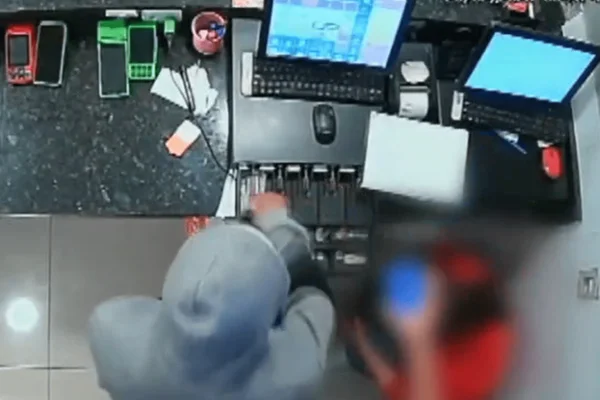 Imagem colorida de uma câmera de segurança mostra um homem encapuzado roubando dinheiro e celulares no caixa de uma pizzaria - Metrópoles