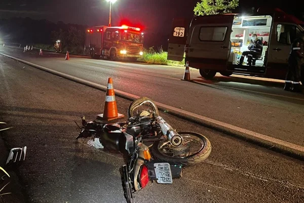 Moto caída em asfalto e ambulância ao fundo