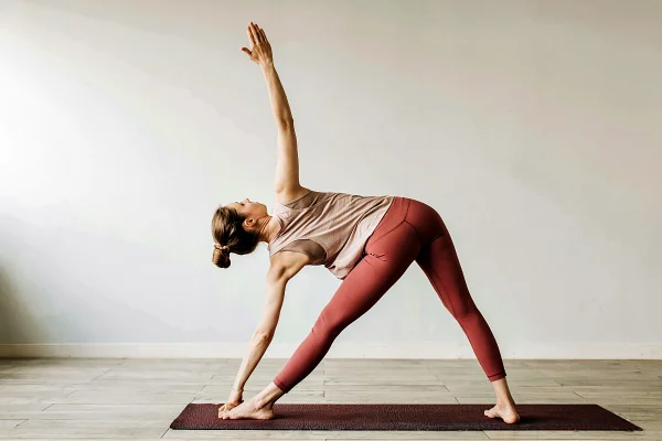 Na foto uma mulher está em cima de um tapetinho de exercício fazendo uma posição do yoga - Metópoles
