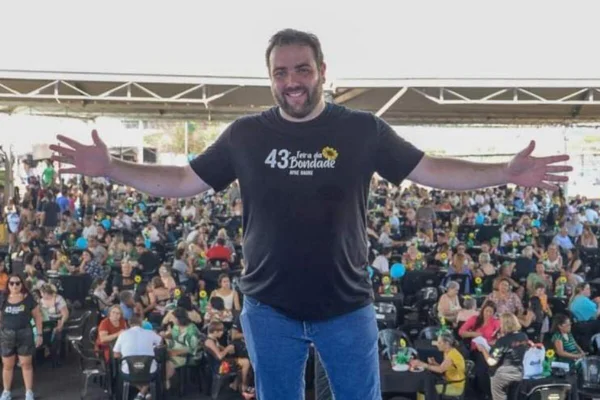 Homem branco , com ambos os braços abertos, sobre palco, com multidão ao fundo, em dia ensolarado - Metrópoles