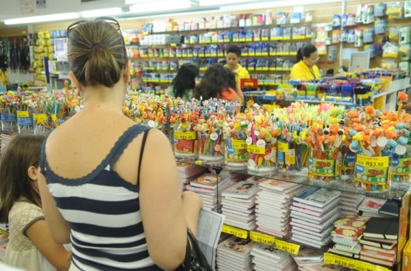 Fotografia colorida de uma mulher escolhendo material escolar - GDF - cartão material escolar