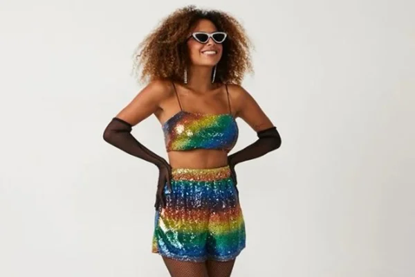 Modelo usa top e short coloridos com brilho, além de óculos escuros e luvas longas pretas. Na imagem, ela está com as mãos apoiadas na cintura - Metrópoles