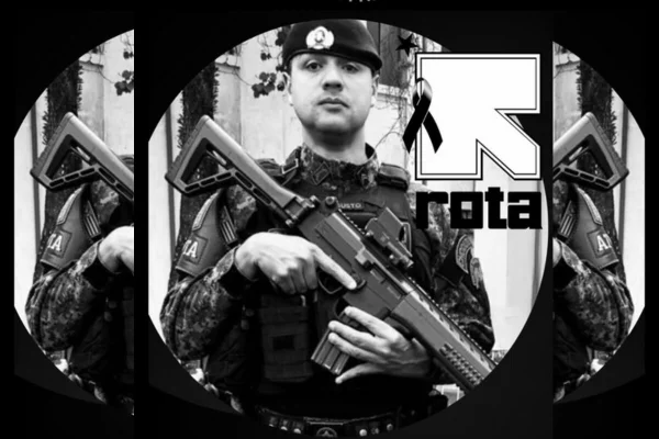 Foto preto e branco de policial fardado, segurando um fuzil atravessado em frente ao peito, ao lado do qual há o símbolo da Rota, da PM de São Paulo - Metrópoles