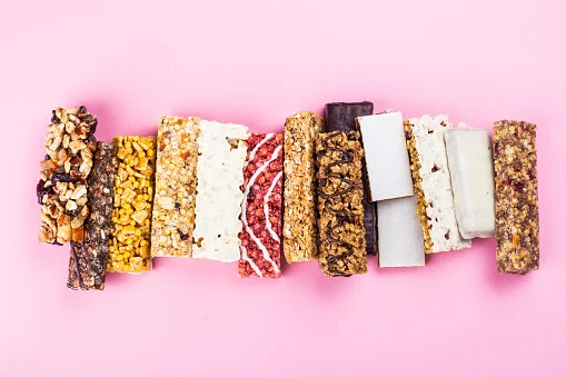 Diversas barras de cereal alinhadas ao lado uma da outra em um fundo rosa