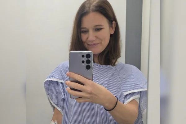 Foto colorida de mulher com roupa de paciente em ambiente hospitalar - Metrópoles