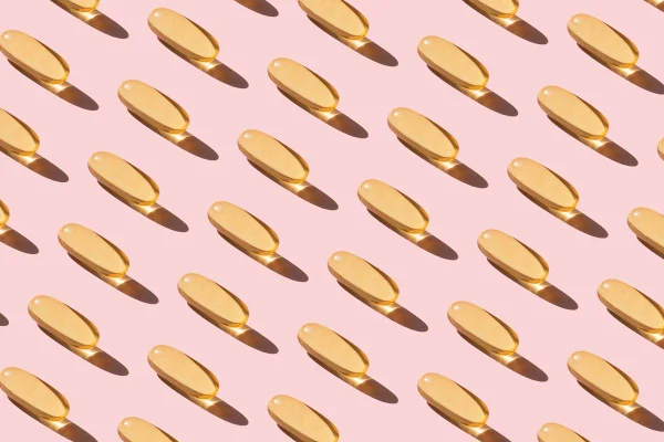 cápsulas de vitamina D em fundo rosa