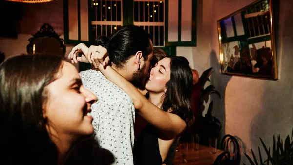 Foto colorida de um casal se beijando em uma festa - Metrópoles