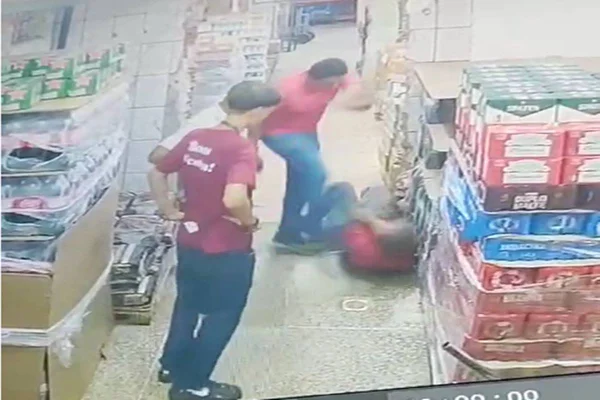 Foto colorida de homem chutando outro rapaz em meio a corredor