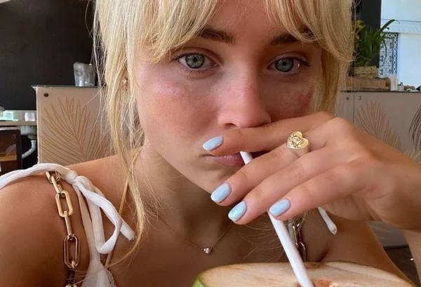 Blueberry milk nails - Mulher loira com canudo na boca mostrando as unhas - Metrópoles