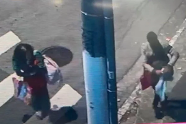 Casal carregando sacolas e bolsas caminha por rua deserta, de noite - Metrópoles