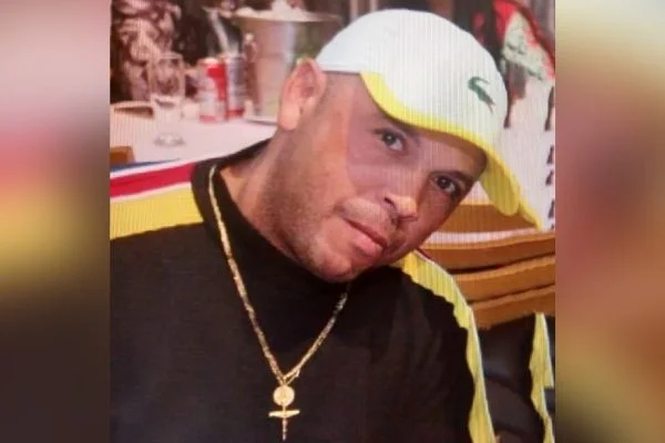 Imagem colorida mostra homem suspeito de ataque a policiais no litoral. Ele é pardo e veste boné branco, blusa preta com detalhes em amarelo e vermelho nos ombros e corrente de ouro no pescoço - Metrópoles
