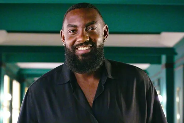 foto colorida de homem negro de barba sorrindo vestindo uma blusa preta - metrópoles