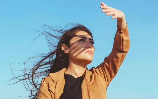 Uma mulher no sol com a mão no rosto