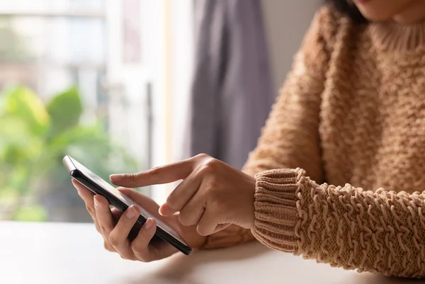 Imagem mostra uma mulher de casaco marrom mexendo no celular com um dedo - Metrópoles