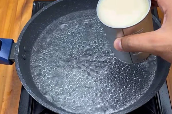 na foto vemos uma frigideira com agua fervendo e uma mao segurando uma lata de leite condensado