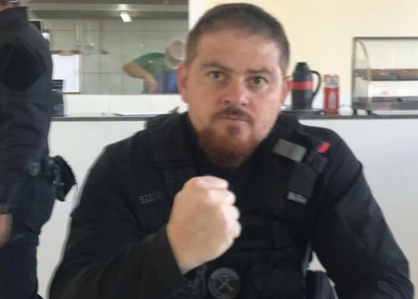 Homem branco com barba e com roupa preta mostrando o punho fechado