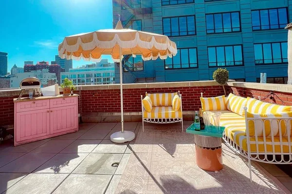 Foto colorida da varanda de um apartamento em Nova York com poltronas amarelas e uma churrasqueira cor de rosa - Metrópoles