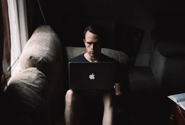 Homem sentado no sofá com macbook no colo, trabalhando