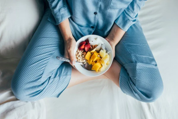 Imagem colorida de pessoa na cama com tigela de frutas