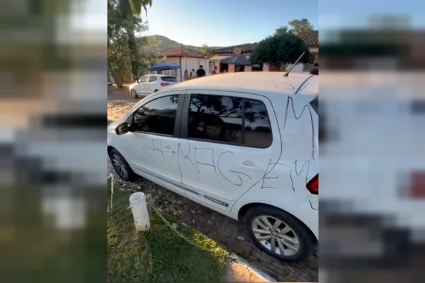 Imagem colorida de um carro branco pichado com a palavra "Garagem"