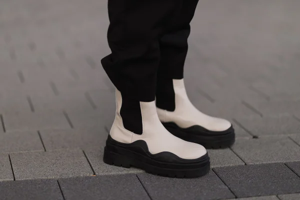 Foto de uma pessoa usando uma bota na rua. O calçado é de couro, na cor branca, com detalhes e o solado tratorado em preto.