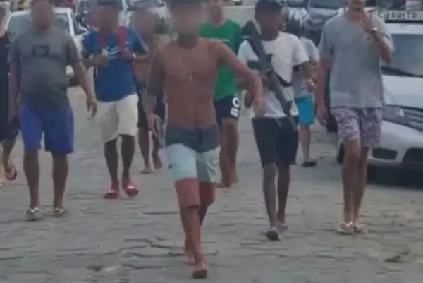 Imagem colorida mostra homens com rostos borrados caminhando em rua portando armas de fogo - Metrópoles