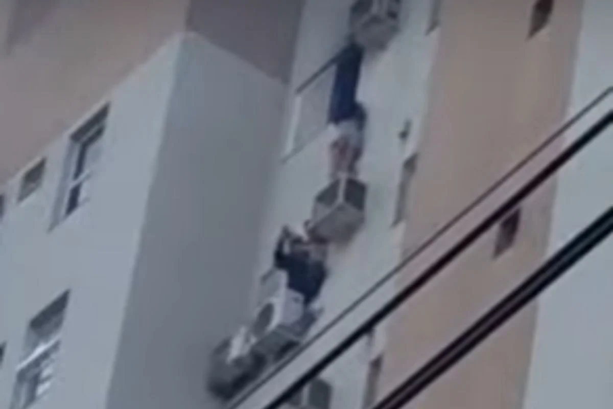 Foto colorida de mulher pendurada em suporte de ar-condicionado - Metrópoles