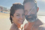 Bárbara Borges e Iran Malfitano posam juntos e sorridentes na praia
