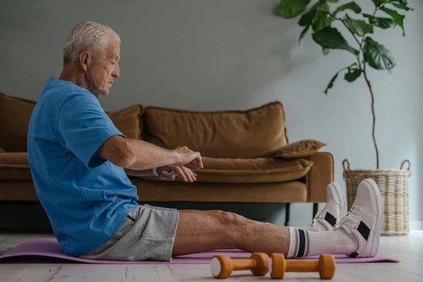 Foto colorida de homem sentado em tapete de treino e ao lado de haltere - Metrópoles