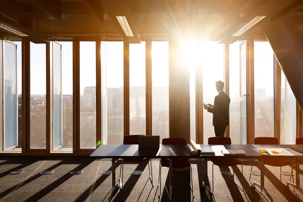 Foto colorida de homem em escritório de frente à janela sob luz natural do sol - Metrópoles.