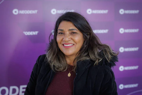 Imagem colorida de mulher vestida com casaco em fundo roxo enquanto sorri - Metrópoles
