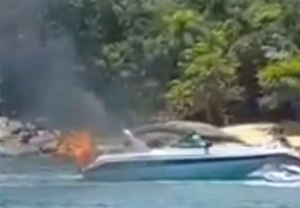 Imagem colorida de lancha com fogo e fumaça no mar com vegetação ao fundo em ubatuba - Metrópoles
