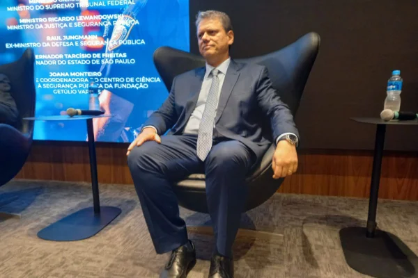 Imagens coloridas mostram o governador de SP, Tarcísio de Freitas, homem branco, com terno escuro e gravata azul clara, sentado em cadeira, ao lado esquerdo um painel
