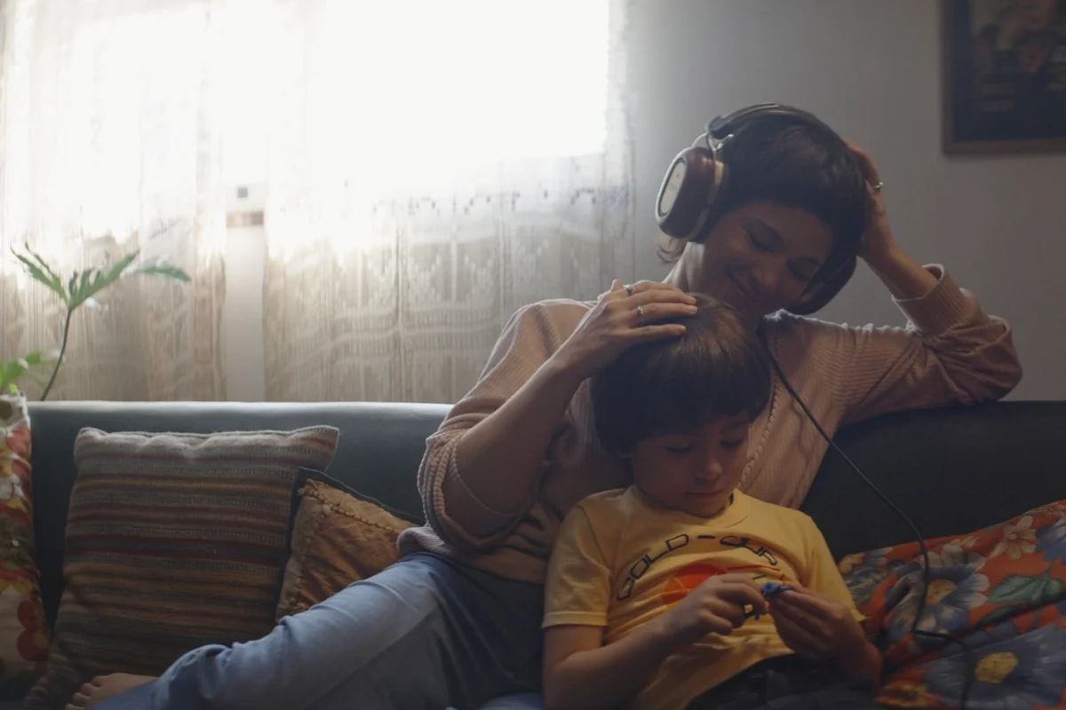 foto colorida de mulher sentada em sofa ouvindo musica com menino -metrópoles