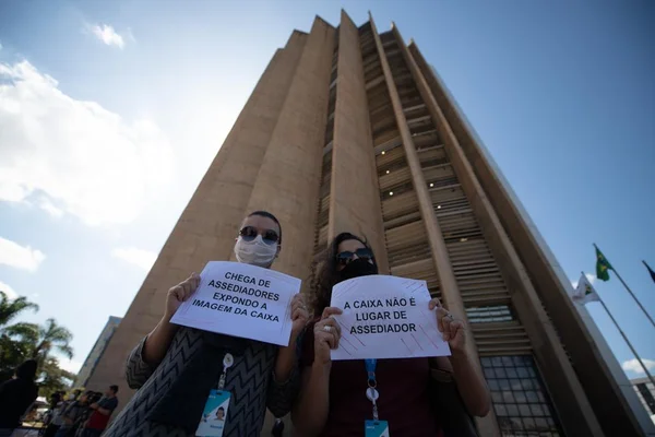 mulheres de preto com com placas brancas na mão, atrás o prédio da caixa