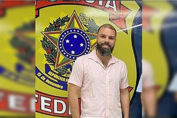 homem de barba sorrindo atrás de brasão da PF