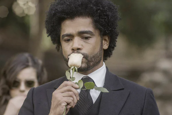 homem negro de terno beija rosa em funeral - metrópoles